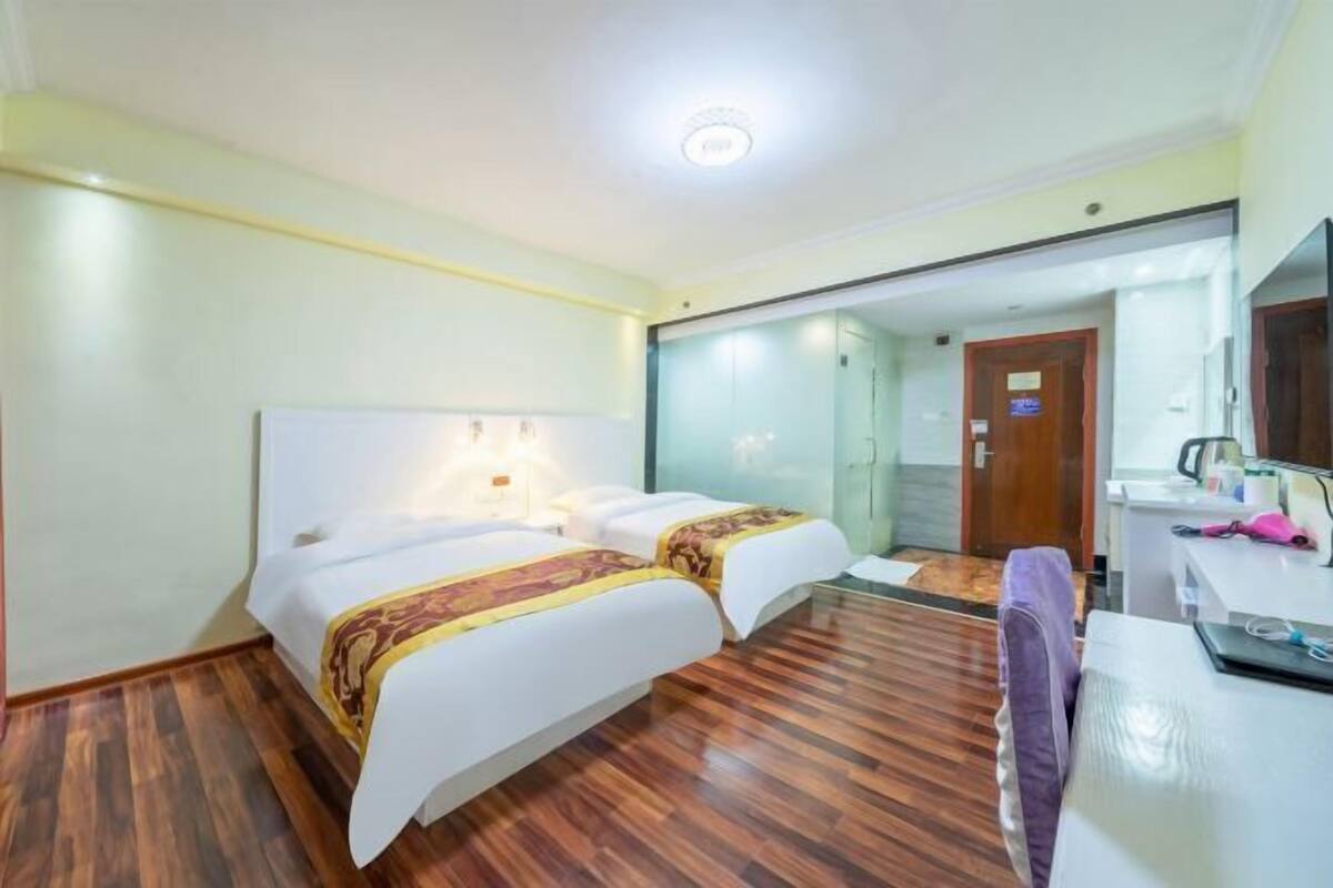 A hotel room with two beds, a desk, a mirror, and a shower area.