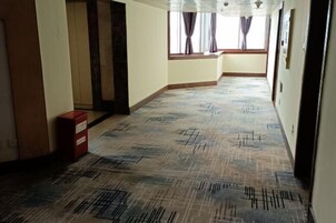 Un pasillo con alfombra estampada, un armario rojo y una ventana con cortinas.