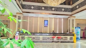 Zona de recepción de hotel con suelo de mármol, mostrador de recepción, pantalla digital y una gran lámpara de araña.