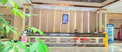 Zona de recepción de un hotel con suelo de mármol, mostrador y una lámpara de araña grande.