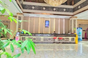 Zona de recepción de un hotel con suelo de mármol, mostrador y una lámpara de araña grande.