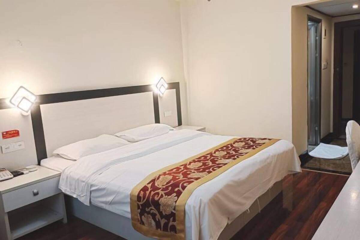 A hotel room with a single bed, a nightstand with a phone, and two wall-mounted lights.