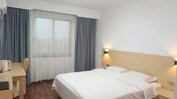 A hotel room with a bed, bedside table, lamp, and a window with curtains.
