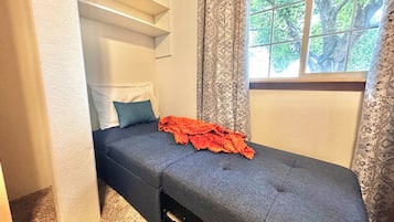 Una stanza piccola e funzionale con un letto singolo, una finestra con tende e una pratica libreria a muro.