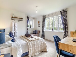 Ein Schlafzimmer mit zwei Betten, einem Fenster mit Vorhängen, einem Nachttisch und einem Sessel.