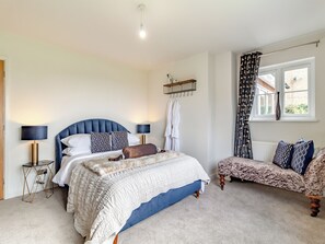 A bedroom with a bed, bedside tables, a chair, a window, and a hanging light fixture.