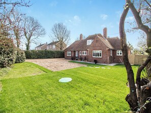 A brick house with a well-maintained lawn, a circular garden feature, and a wooden fence.