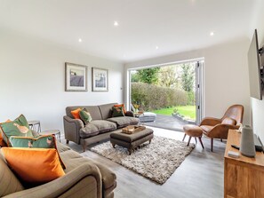 A modern living room with a sofa, ottoman, and chairs, a rug, and a view of a garden through a glass door.