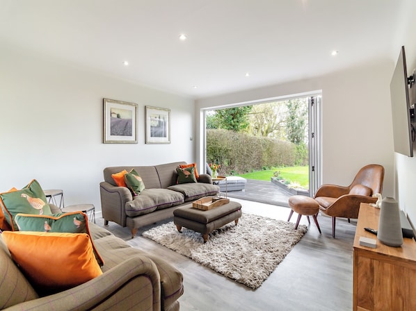 A modern living room with a sofa, ottoman, and chairs, a rug, and a view of a garden through a glass door.