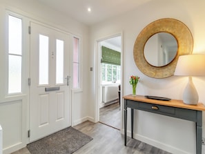 A hallway with white doors, a round mirror, a desk with a lamp, and a vase of flowers.