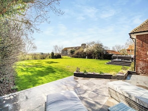 A patio with outdoor furniture, a grassy yard, and a brick building in the background.