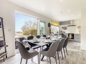 A modern dining area with a table set for four, a kitchen with white cabinets, and a view of the outdoors.