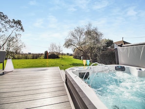 A hot tub on a wooden deck with a grassy yard and trees in the background.