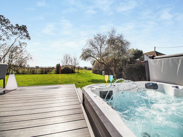 A hot tub on a wooden deck with a grassy yard and trees in the background.