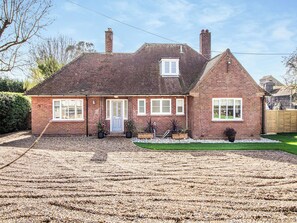 Uma casa de dois andares em tijolos, com varanda frontal, um pequeno jardim e uma entrada de automóveis com calçamento de brita.