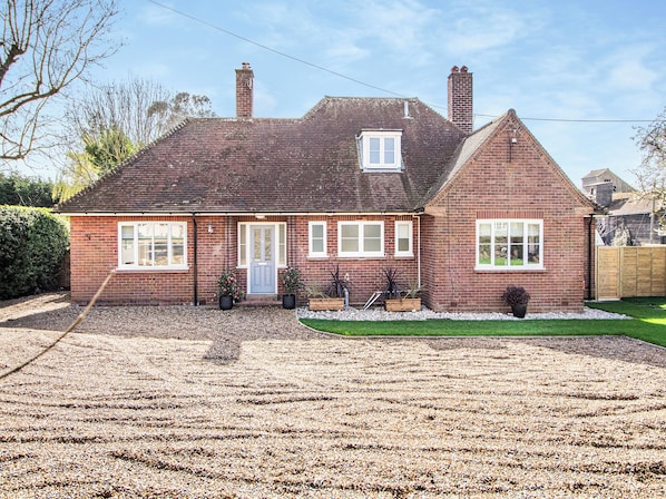 A two-story brick house with a front porch, a small garden, and a gravel driveway.