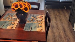 Ein Wohnzimmer mit einer Couch, einem Esstisch mit einer Vase voller Sonnenblumen und einem schwarzen Ledersofa.