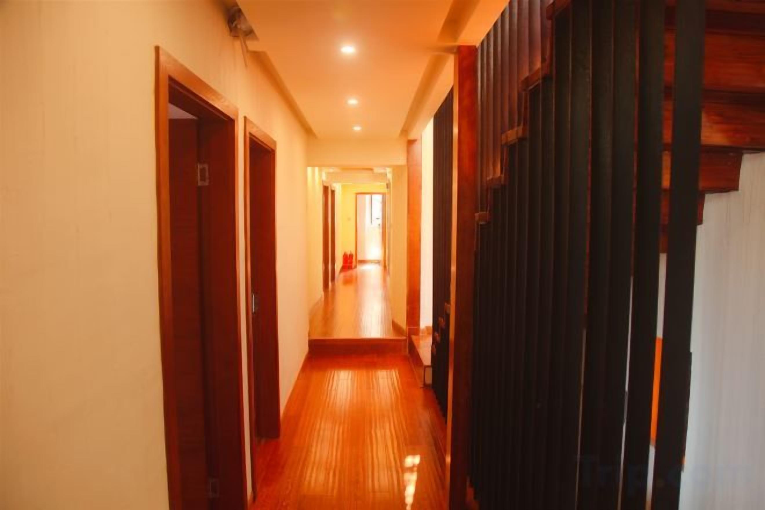 A corridor with wooden flooring and doors on both sides, leading to a bright room at the end.