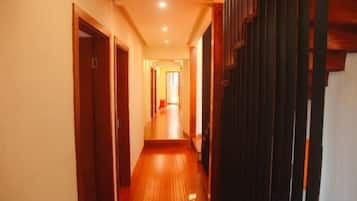 A corridor with wooden flooring and doors on both sides, leading to a bright room at the end.