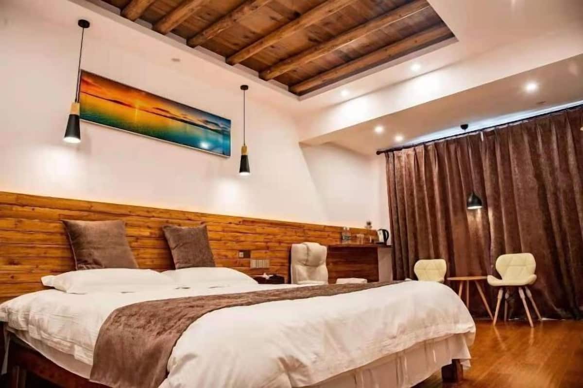 A bedroom with a wooden headboard, a large bed, a painting, a desk, and a chair.