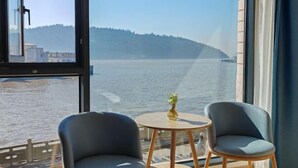 A room with a large window overlooking a body of water and a distant hill. There are two chairs and a small round table with a pineapple on it. - Tinghai Guesthouse (Yuhuan)