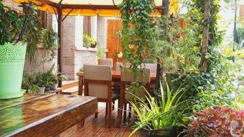 An outdoor patio with a wooden table and chairs, surrounded by potted plants and a hanging plant.