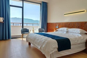 A hotel room with a large bed, a view of the outdoors, a small table, and a chair. - Tinghai Guesthouse (Yuhuan)