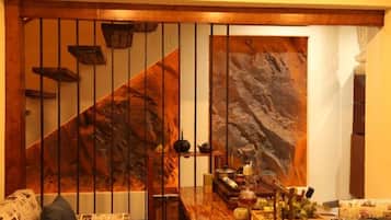 Una habitación con una escalera de madera, una gran obra de arte en forma de roca y una mesa de comedor con varios objetos.