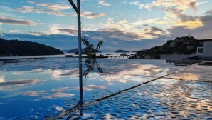 A waterfront view with a metal railing, calm water, and distant hills. - Tinghai Guesthouse (Yuhuan)