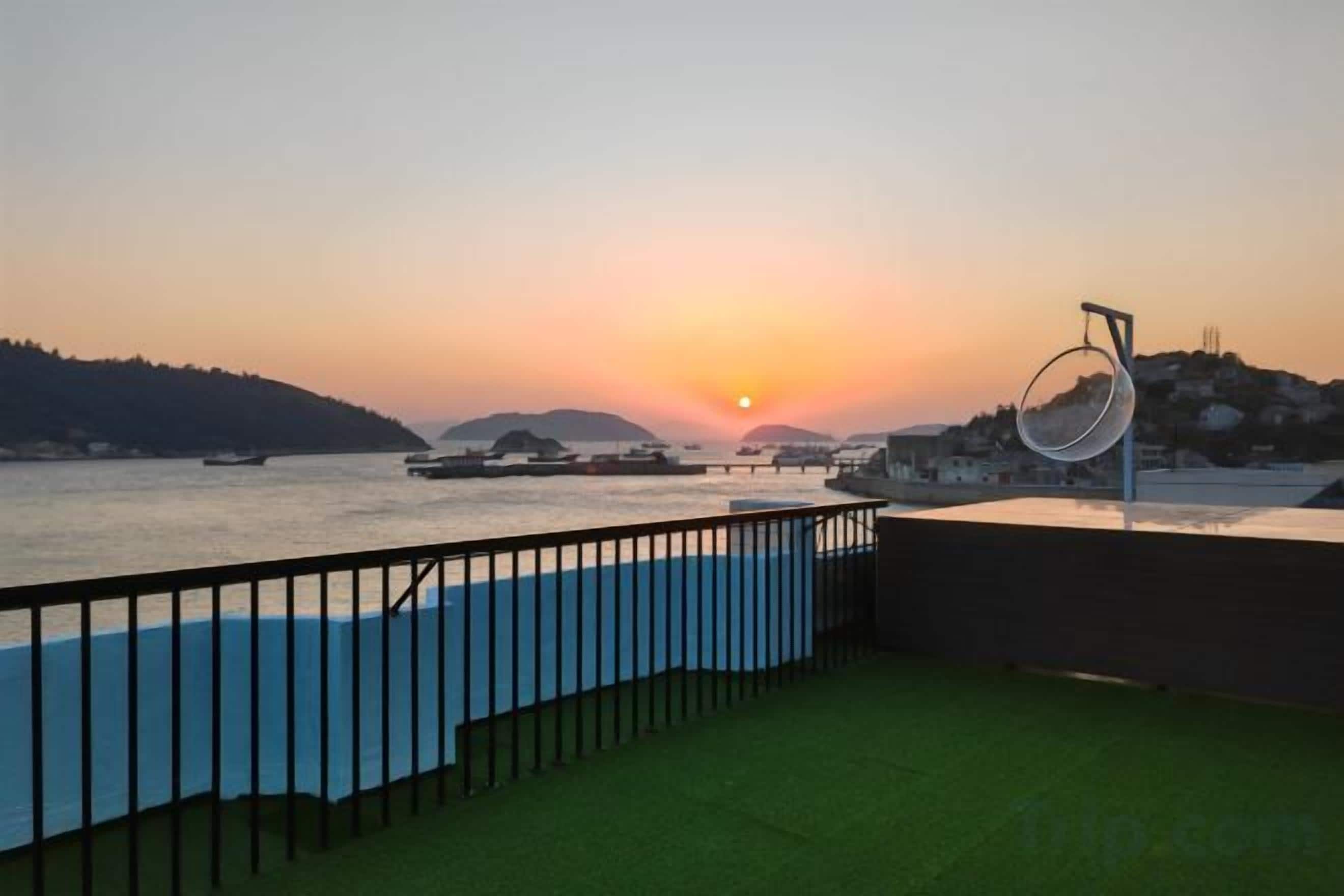 A waterfront view with a sunset, boats, and a circular structure.