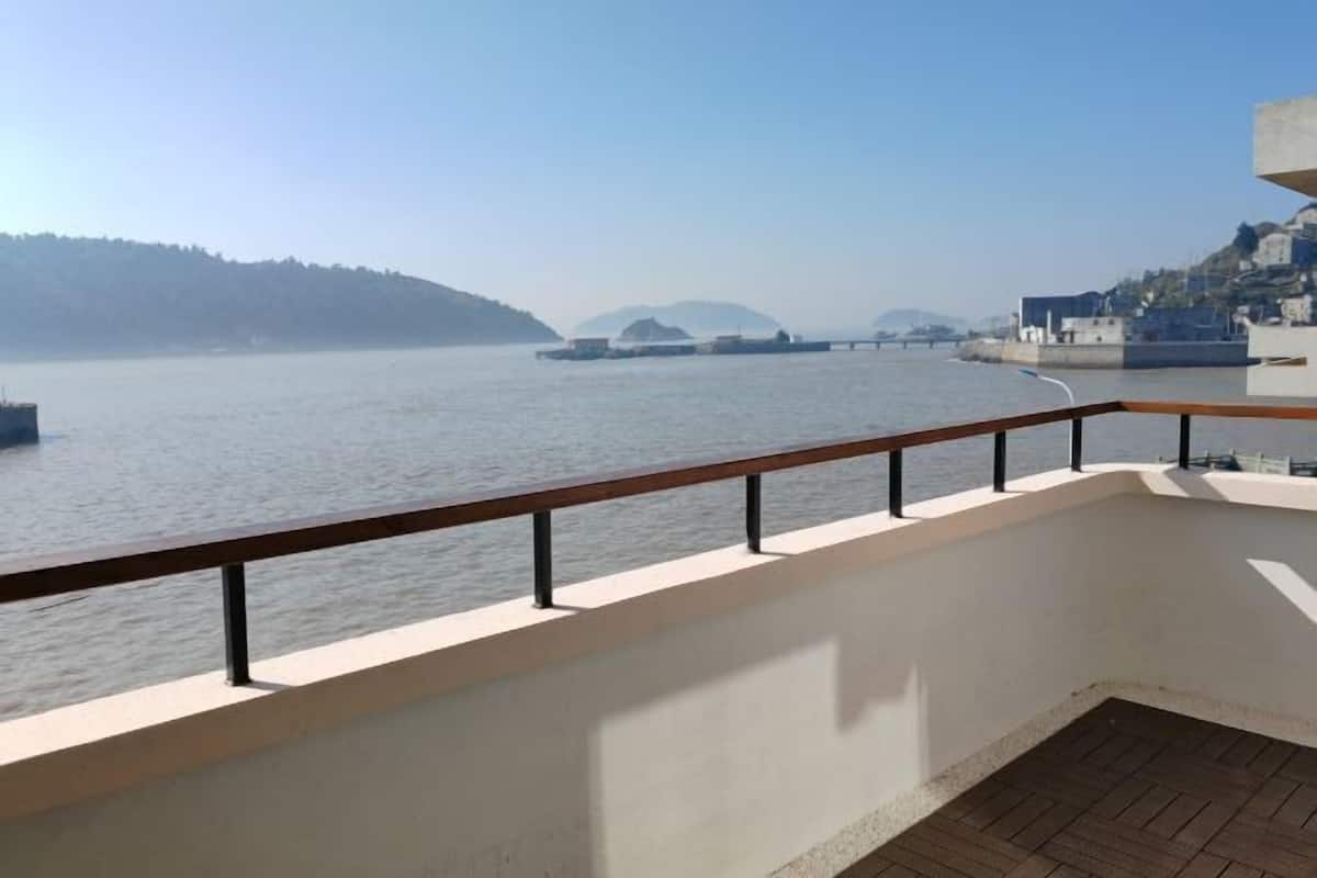A balcony with a view of a calm body of water, a distant bridge, and a hilly landscape.