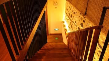 A wooden staircase with a metal railing leading to a room with a patterned wall and a green exit sign.