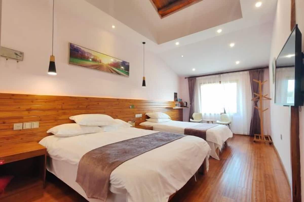 A hotel room with two beds, wooden headboard, a painting, a TV, and a window with curtains.