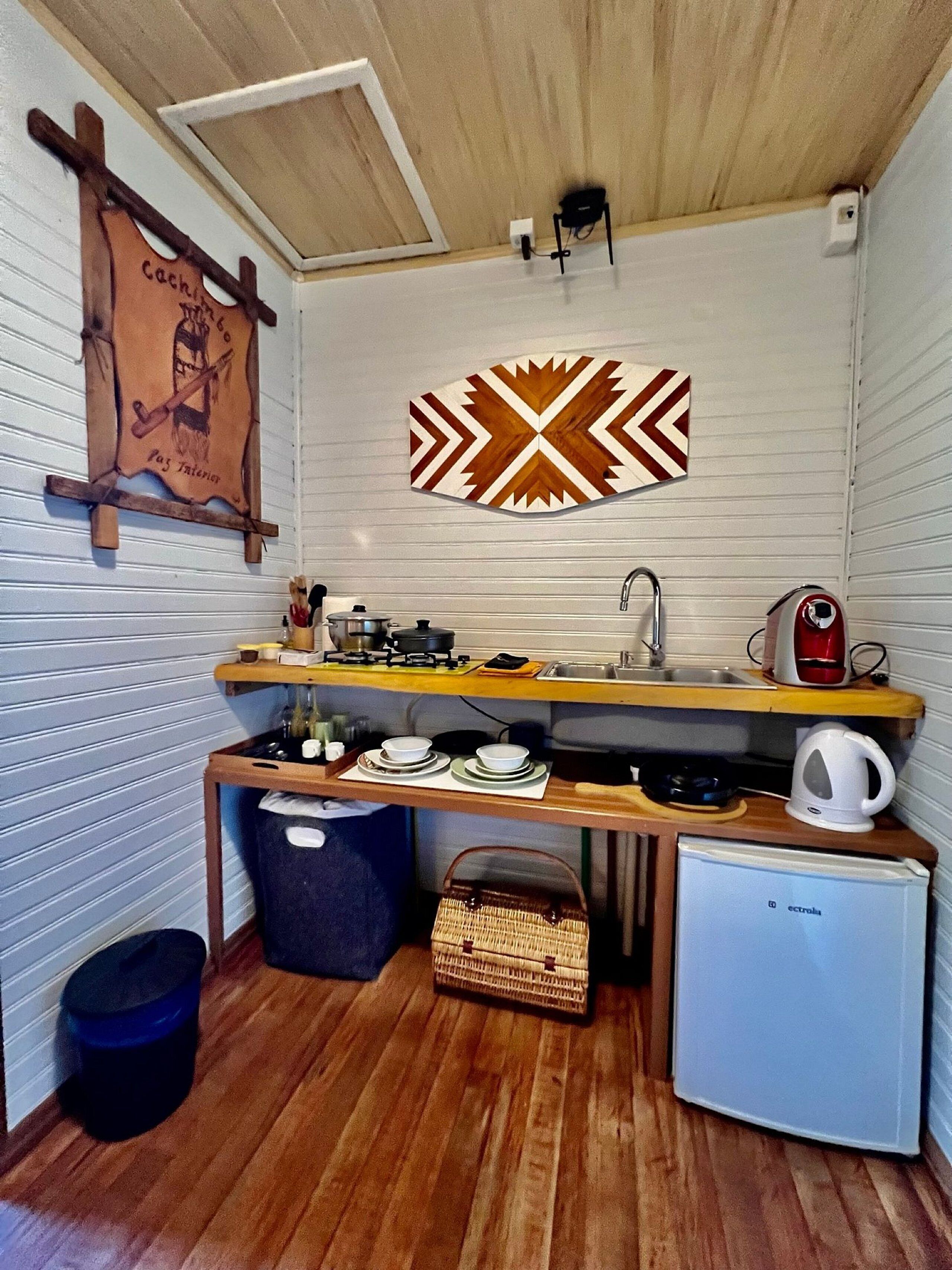 Uma cozinha compacta com bancada de madeira, pia, pequena geladeira e um objeto decorativo na parede.