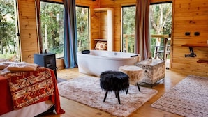 A wooden cabin room with a bed, a large bathtub, and a small stool. - Cabanas Cambuim - Urubici - SC (Urubici)