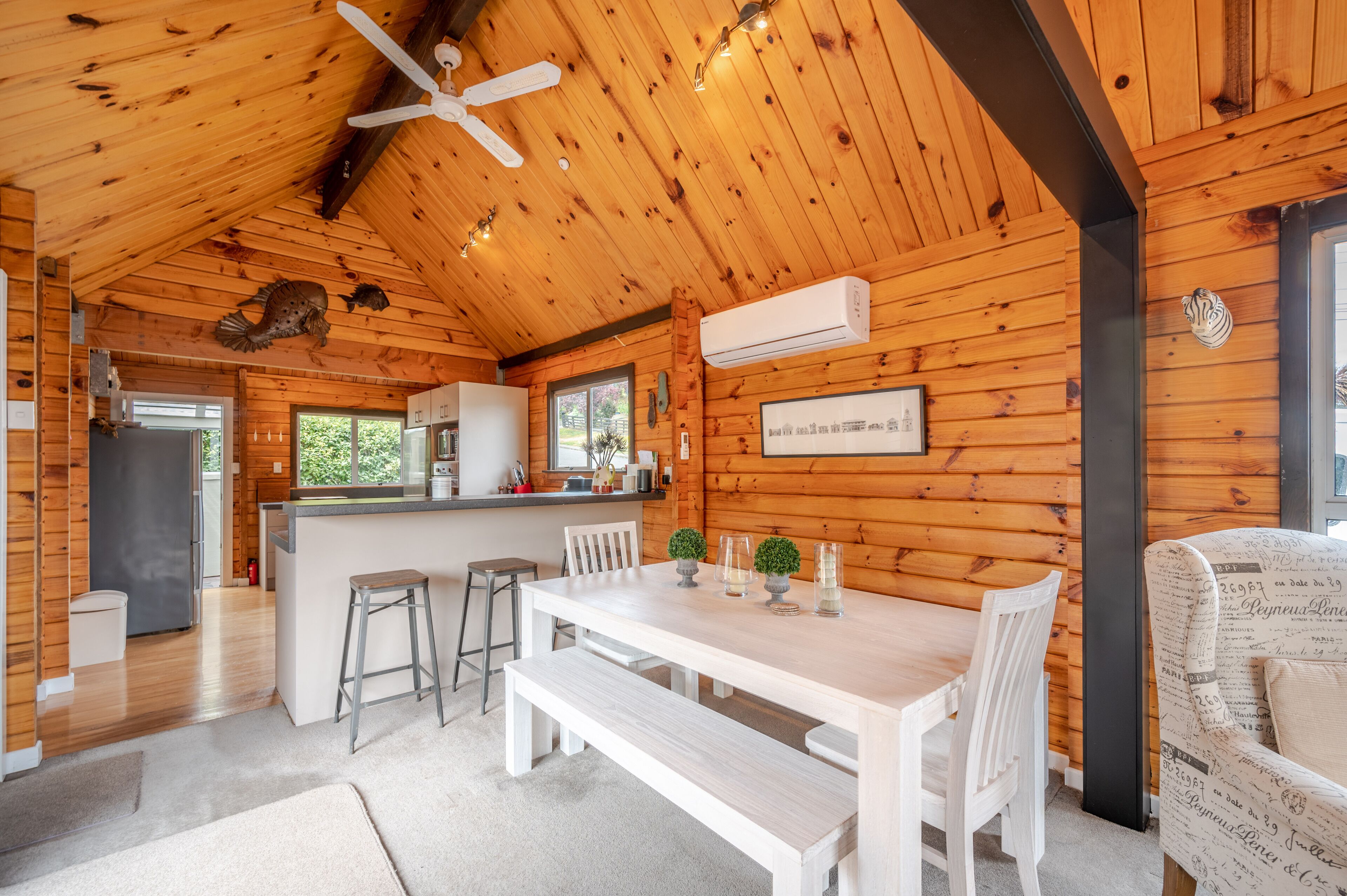 A wooden cabin interior with a dining area, kitchen, and a ceiling fan.