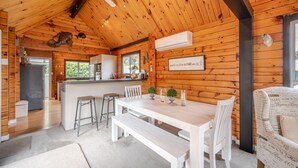 A wooden cabin interior with a dining area, kitchen, and a ceiling fan.