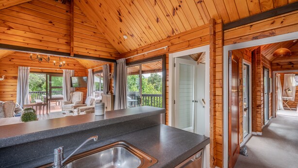 A wooden cabin interior with a kitchen area, dining space, and a view of the outdoors.