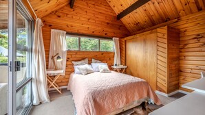 A wooden cabin bedroom with a large bed, a small table, and a chair.