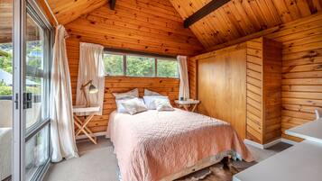 A wooden cabin bedroom with a large bed, a small table, and a chair.