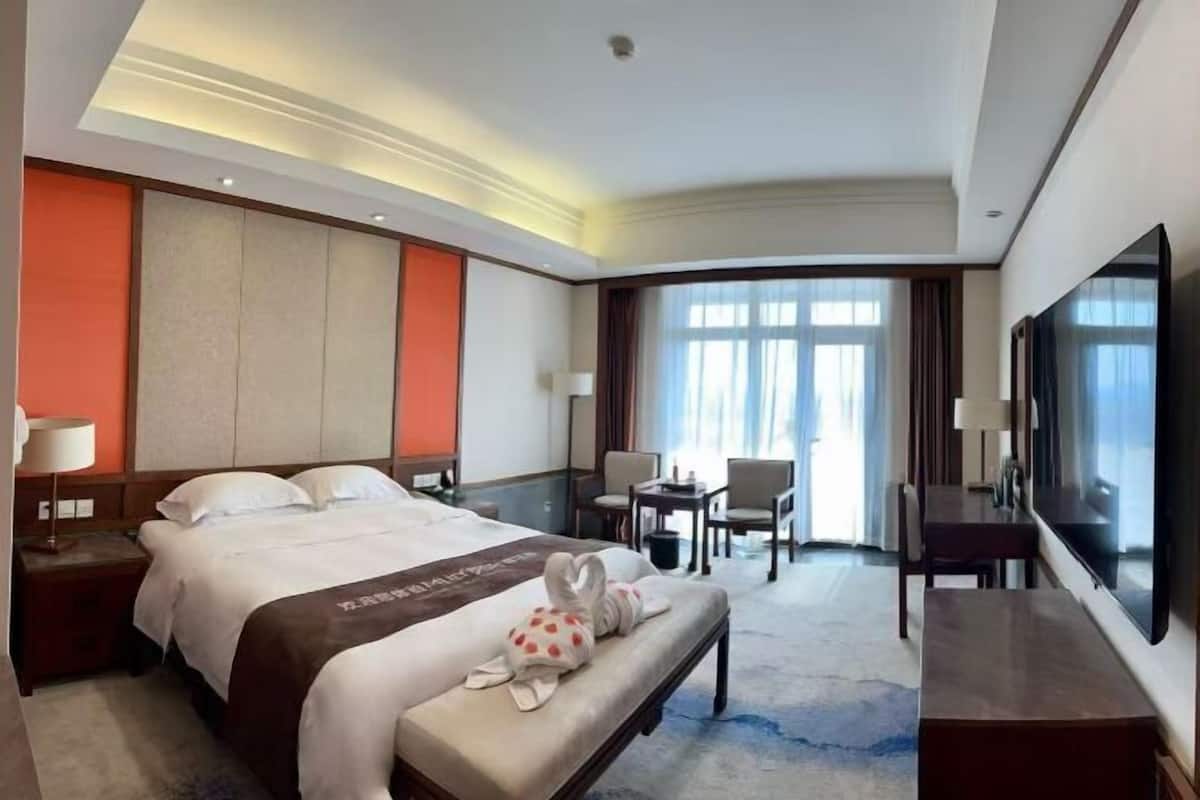 A hotel room with a large bed, a desk, a chair, a TV, and a window with curtains.