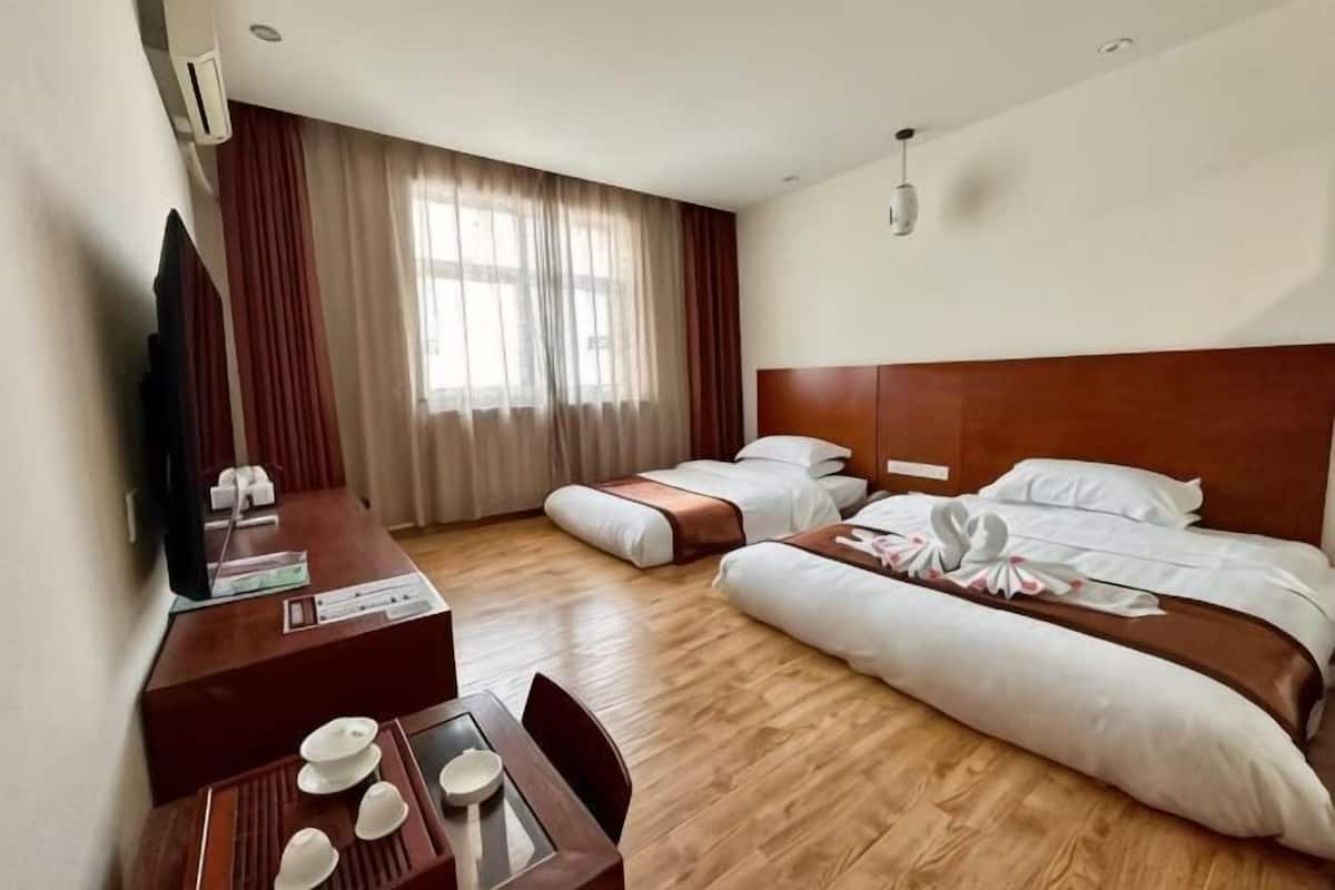 A hotel room with a wooden floor, a desk with a chair, a bed with white bedding, a television on the desk, and a window with curtains.