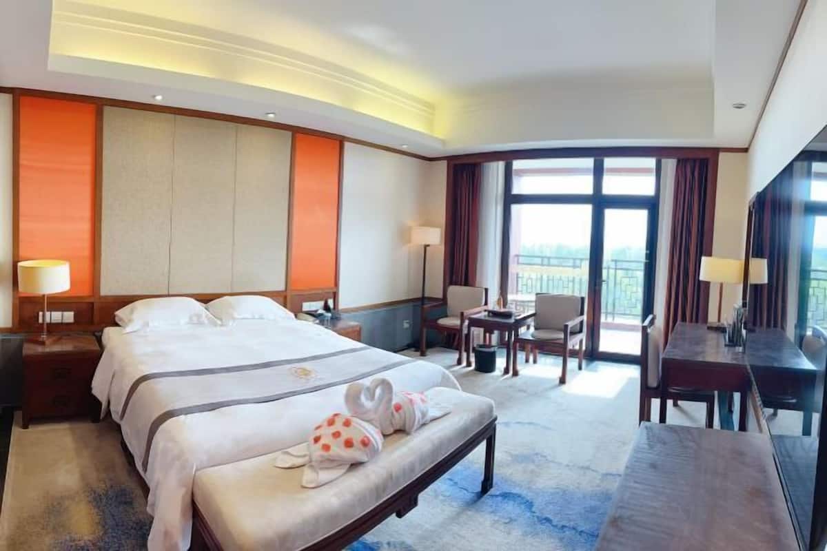 A hotel room with a large bed, a desk, and a chair. There is a balcony with a view.