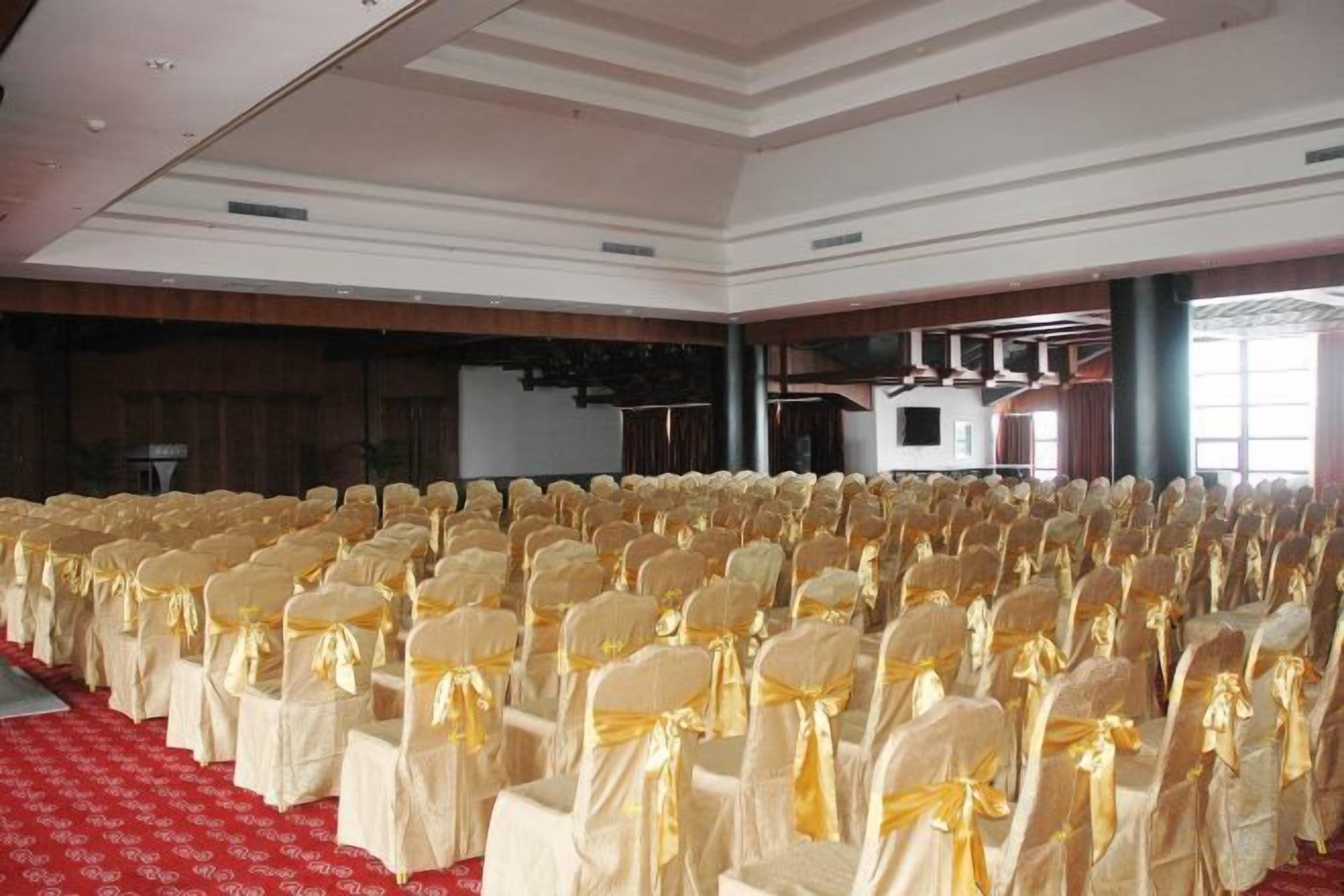 A large hall with rows of chairs covered in white and gold, a red carpet, and a stage with a screen.