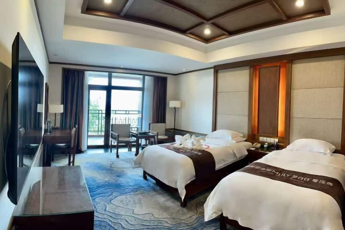 A hotel room with two beds, a desk, a chair, and a large window.