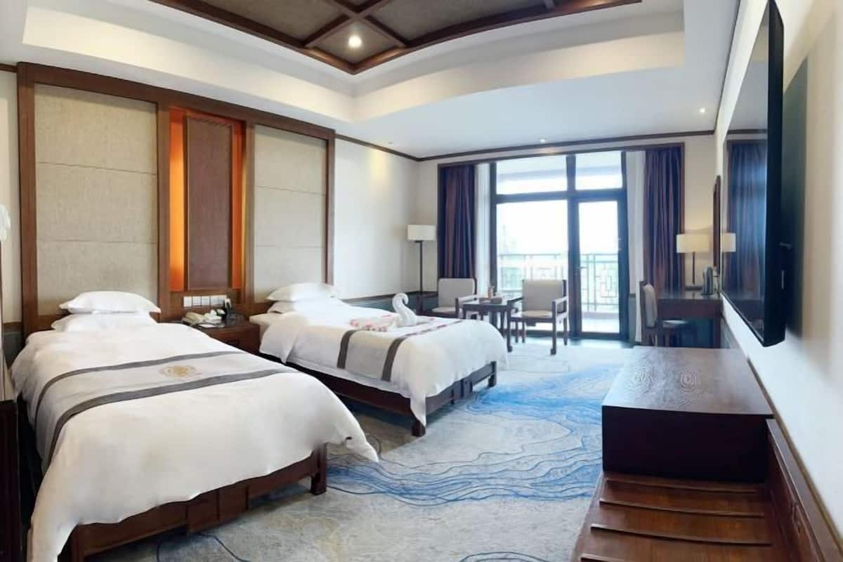 A hotel room with two beds, a desk, a chair, and a large window.