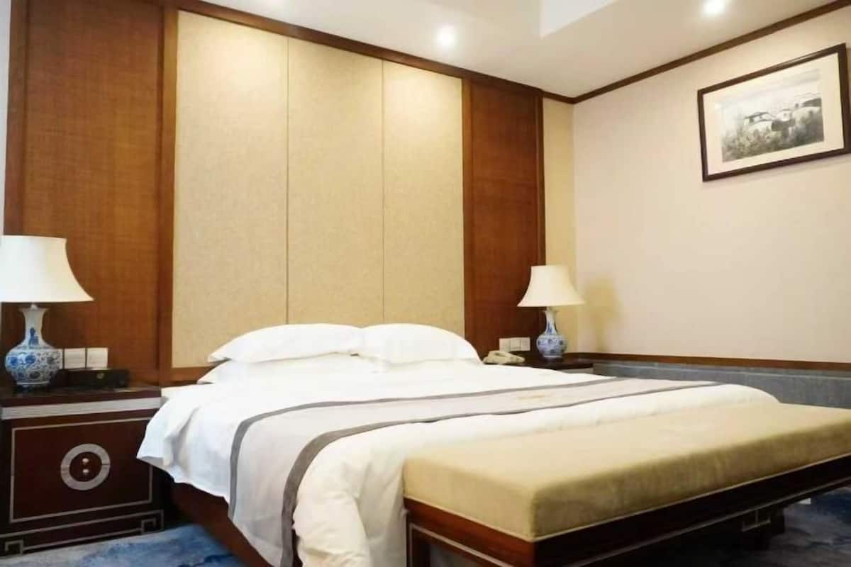 A hotel room with a bed, two bedside tables with lamps, a wall-mounted telephone, and a framed picture.