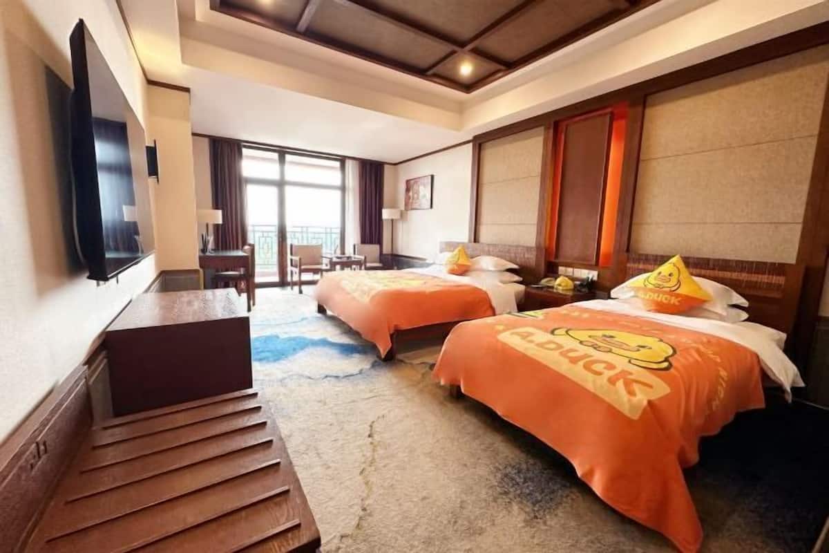 A hotel room with two beds, a desk, a TV, and a view of the outdoors.