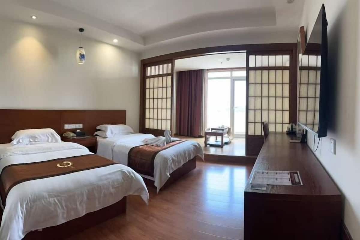 A hotel room with two beds, a desk, a chair, and a sliding door leading to a balcony.
