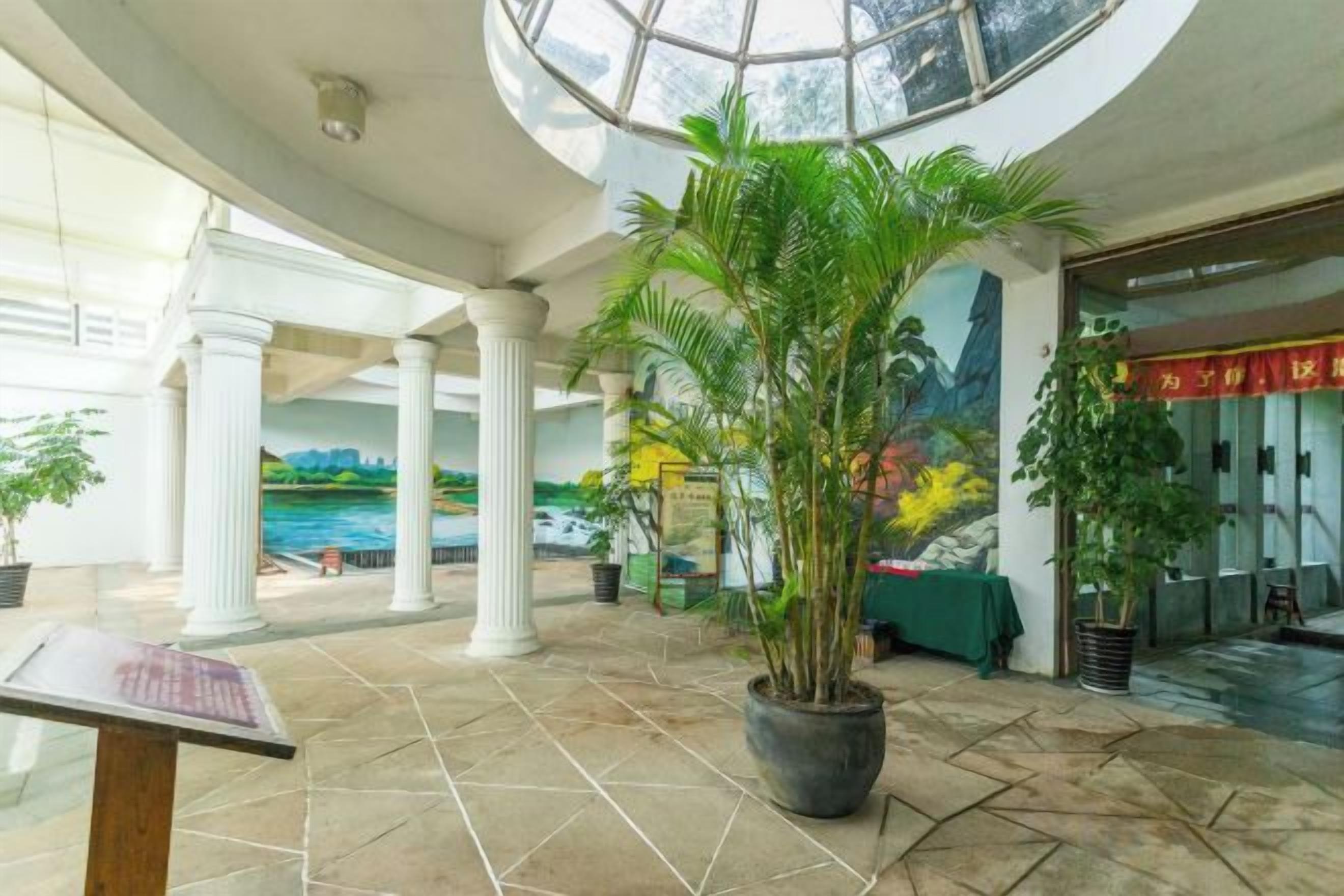 A lobby with a large potted plant, a mural, and a glass ceiling.